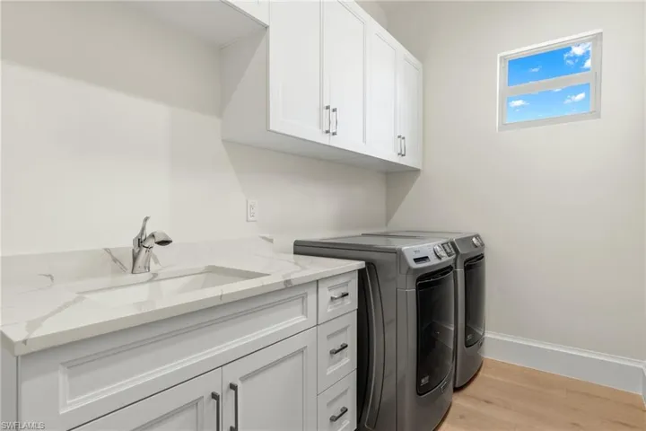 Laundry area featuring cabinets, sink, washing machine and clothes dryer, and light hardwood / wood-style flooring