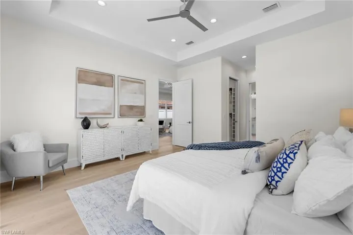 Bedroom with ceiling fan, a tray ceiling, and light wood-type flooring