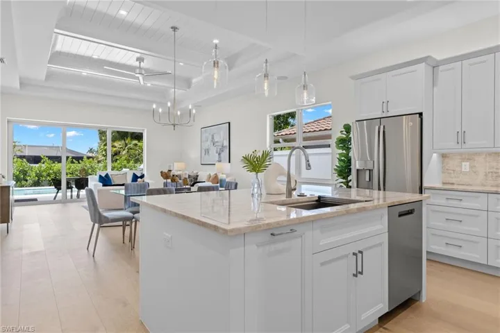 Kitchen with light hardwood / wood-style floors, tasteful backsplash, an island with sink, white cabinetry, and appliances with stainless steel finishes