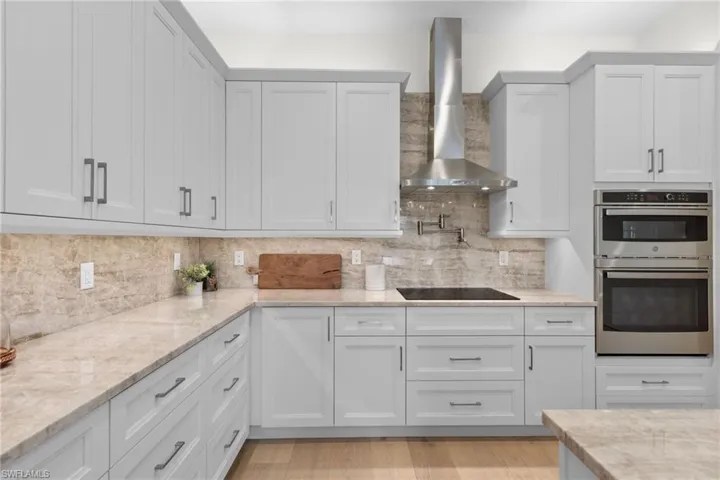 Kitchen with backsplash, wall chimney range hood, stainless steel double oven, and light hardwood / wood-style floors