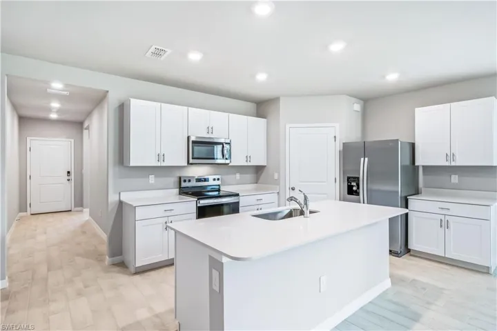 Kitchen featuring white cabinetry, stainless steel appliances, sink, and a center island with sink
