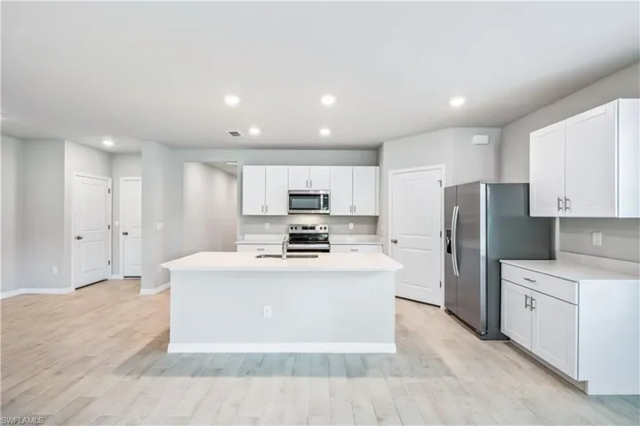 Kitchen featuring a kitchen island with sink, light hardwood / wood-style flooring, stainless steel appliances, sink, and white cabinets