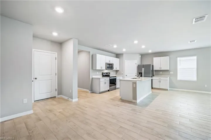 Kitchen with white cabinets, a center island with sink, light wood-type flooring, stainless steel appliances, and sink