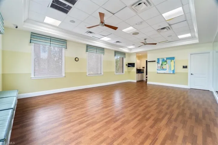 Exercise area with a paneled ceiling, ceiling fan, a raised ceiling, and hardwood / wood-style floors