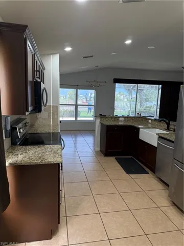 Kitchen featuring dark wood cabinetry, granite countertops, tile flooring, stainless steel appliances, and a farmhouse sink