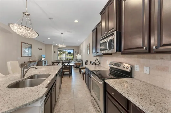 Kitchen with dark brown cabinets, decorative light fixtures, sink, light stone counters, and stainless steel appliances
