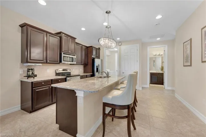 Kitchen with backsplash, a kitchen breakfast bar, a center island with sink, hanging light fixtures, and appliances with stainless steel finishes