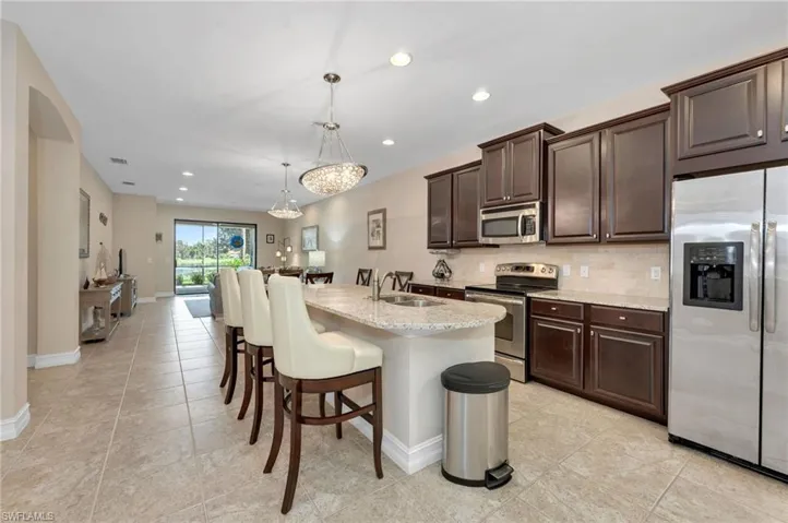 Kitchen with dark brown cabinetry, an island with sink, decorative light fixtures, backsplash, and stainless steel appliances