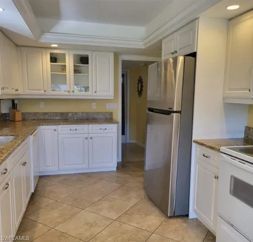 Kitchen with white cabinets, white appliances, a tray ceiling, and crown molding
