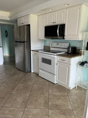Kitchen featuring stainless steel fridge, crown molding, electric stove, white cabinets, and light tile patterned flooring