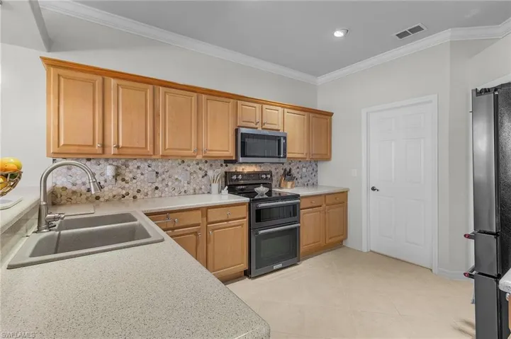 Kitchen with pendant lighting, sink, crown molding, black appliances, and decorative backsplash