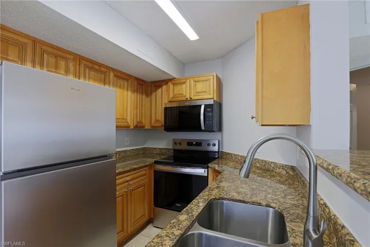Kitchen with stainless steel appliances, dark stone countertops, wood finish cabinetry, and a textured ceiling