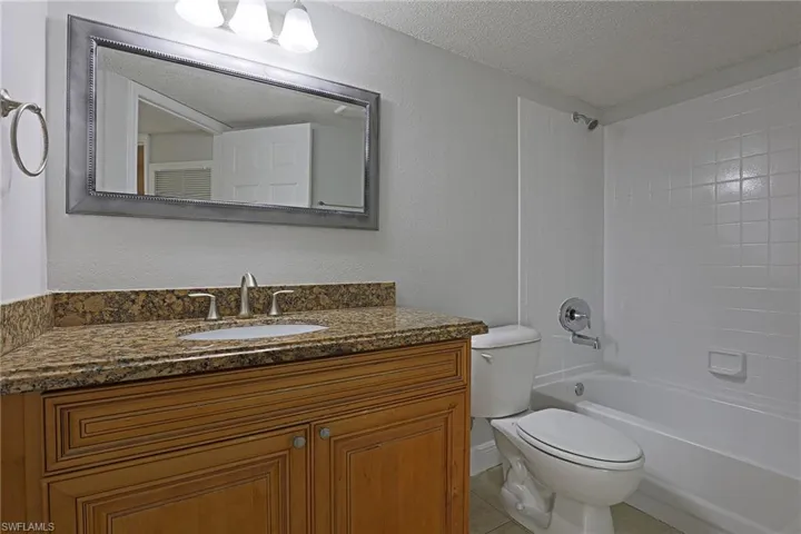 Full bathroom featuring a textured wall, a textured ceiling, vanity, shower / bathtub combination, and light tile patterned floors