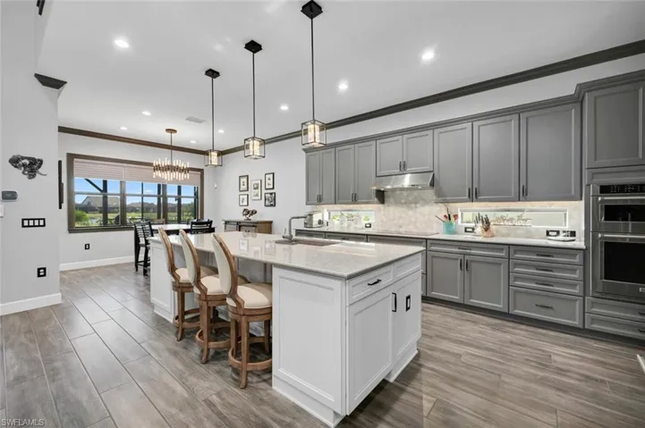 Kitchen with a center island with sink, decorative light fixtures, gray cabinets, and stainless steel double oven