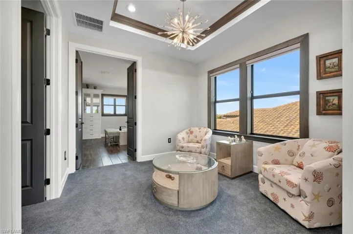 Sitting room featuring a raised ceiling, crown molding, dark carpet, and a notable chandelier