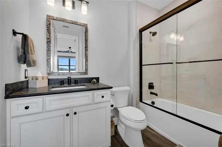 Full bathroom with vanity, toilet, wood-type flooring, and bath / shower combo with glass door