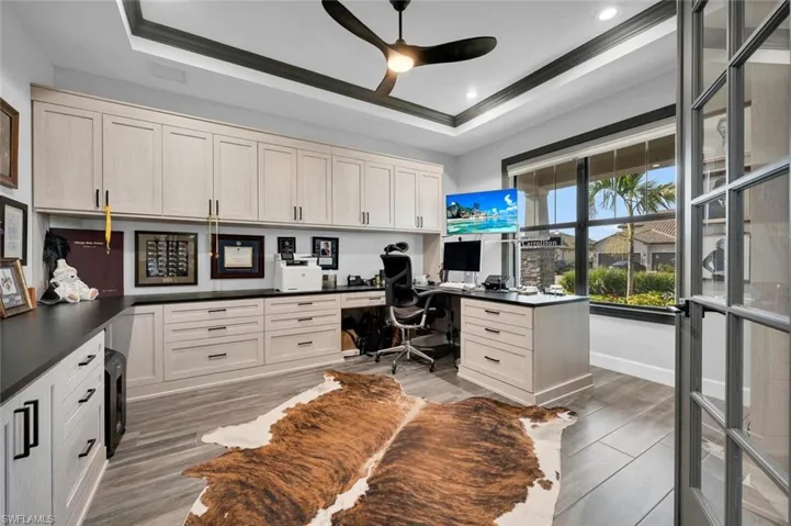 Home office with ceiling fan, dark wood-type flooring, crown molding, a tray ceiling, and built in desk