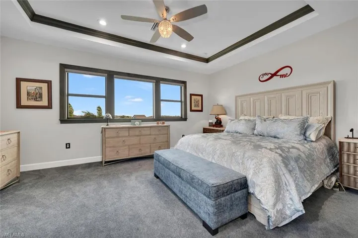 Bedroom with a tray ceiling, ceiling fan, carpet, and ornamental molding