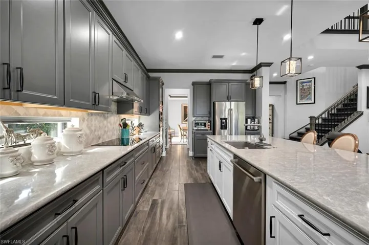 Kitchen featuring stainless steel appliances, dark wood-type flooring, crown molding, sink, and hanging light fixtures