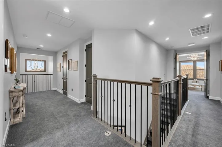 Hallway featuring dark colored carpet and a notable chandelier