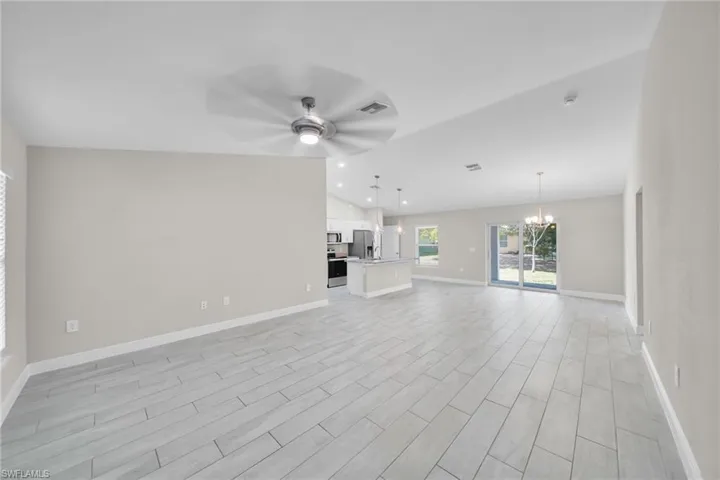 Unfurnished living room featuring a ceiling fan, a chandelier, wood tiled floors, and lofted ceiling