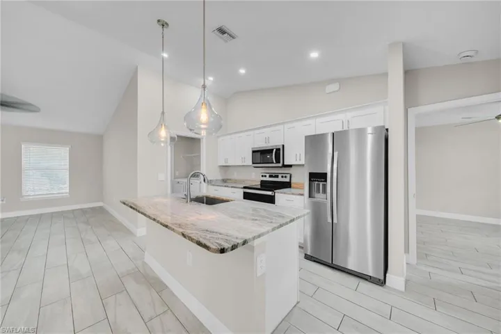 Kitchen featuring stainless steel appliances, a ceiling fan, light stone countertops, vaulted ceiling, and decorative light fixtures