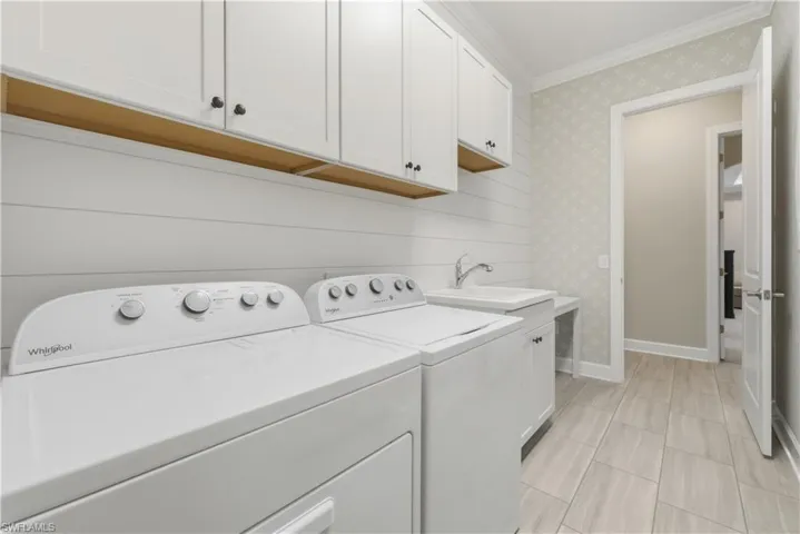 Laundry area featuring crown molding, wallpapered walls, washing machine and clothes dryer, and cabinet space