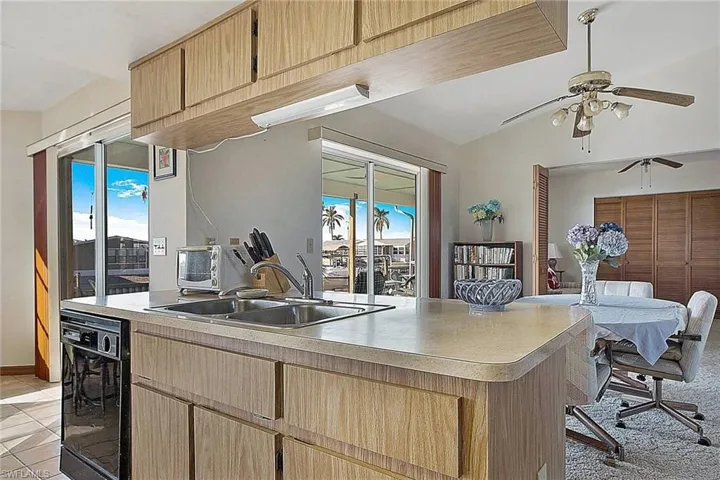 Kitchen featuring ceiling fan, light countertops, light brown cabinets, light tile patterned floors, and vaulted ceiling