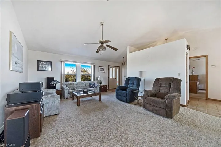 Living room featuring a ceiling fan, vaulted ceiling, carpet, and tile patterned flooring