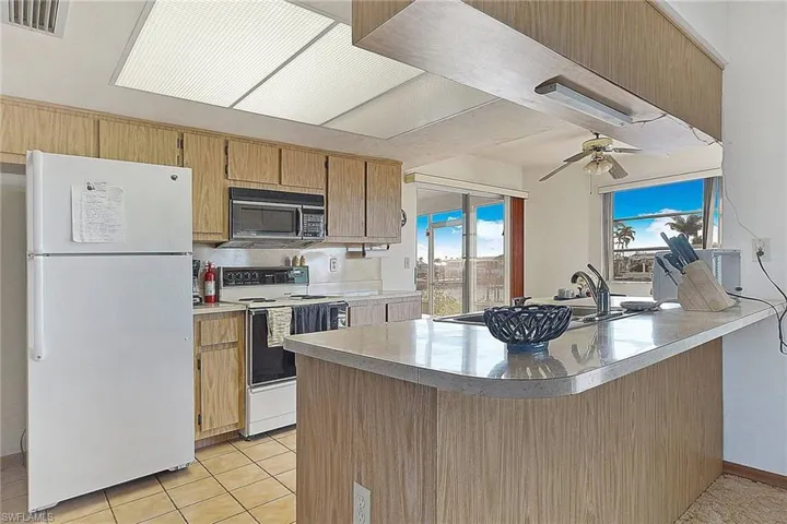 Kitchen featuring white appliances, a peninsula, ceiling fan, light tile patterned flooring, and plenty of natural light