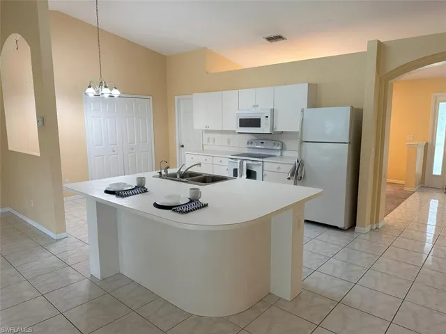Kitchen featuring white appliances, white cabinets, sink, an island with sink, and light tile patterned flooring