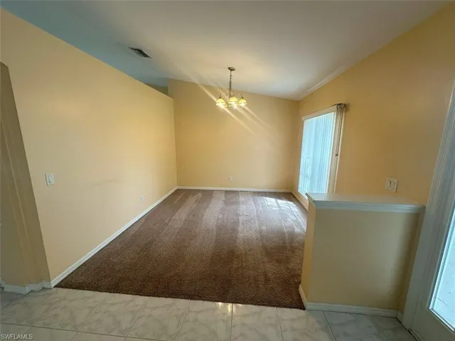 Tiled spare room featuring a notable chandelier and lofted ceiling