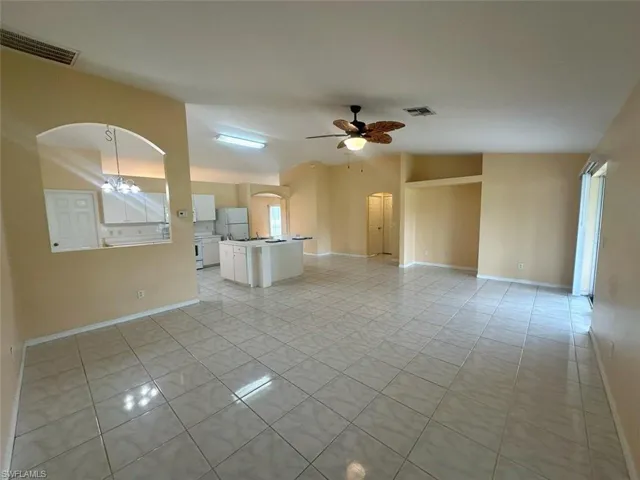 Unfurnished living room with ceiling fan with notable chandelier, vaulted ceiling, and light tile patterned floors