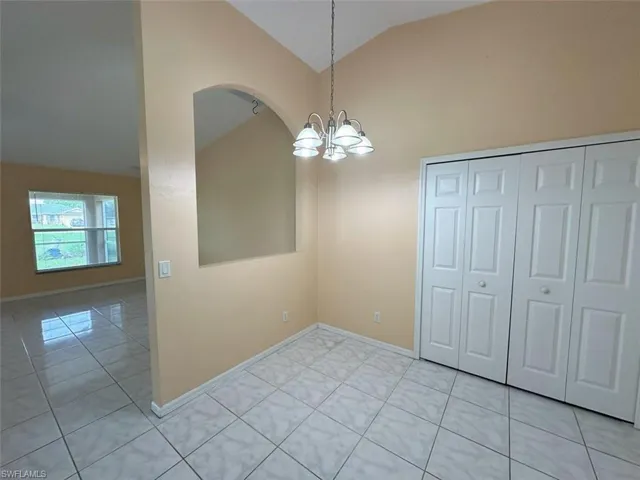 Unfurnished dining area with light tile patterned flooring, a notable chandelier, and high vaulted ceiling
