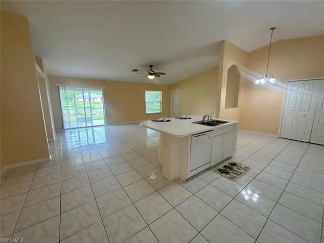 Kitchen featuring white cabinetry, ceiling fan with notable chandelier, dishwasher, lofted ceiling, and a kitchen island with sink