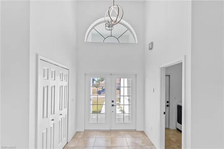 Entrance foyer featuring a high ceiling, french doors, plenty of natural light, light tile patterned floors, and a chandelier
