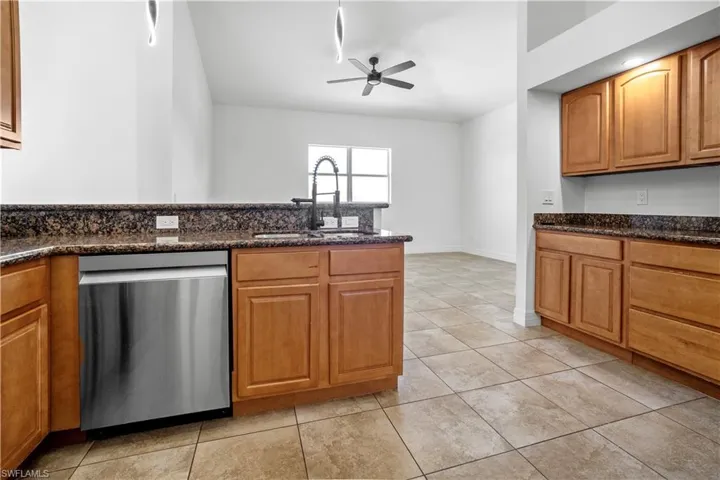 Kitchen featuring wood finish cabinets, stainless steel dishwasher, dark stone countertops, a ceiling fan, and light tile patterned floors