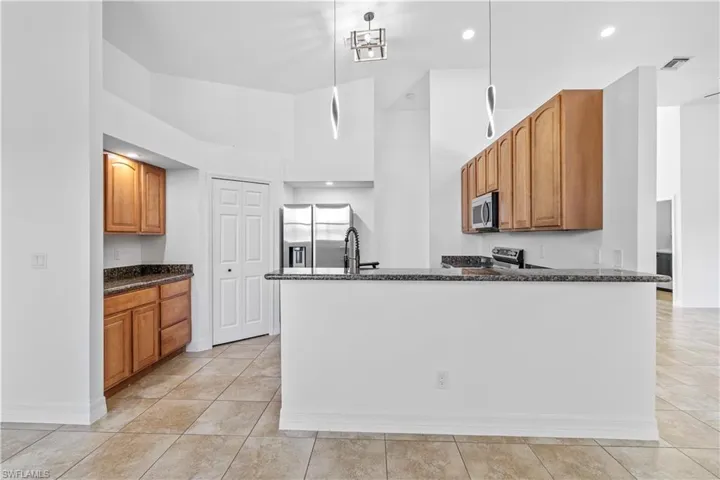 Kitchen with dark stone countertops, a high ceiling, stainless steel appliances, wood finish cabinets, and decorative light fixtures