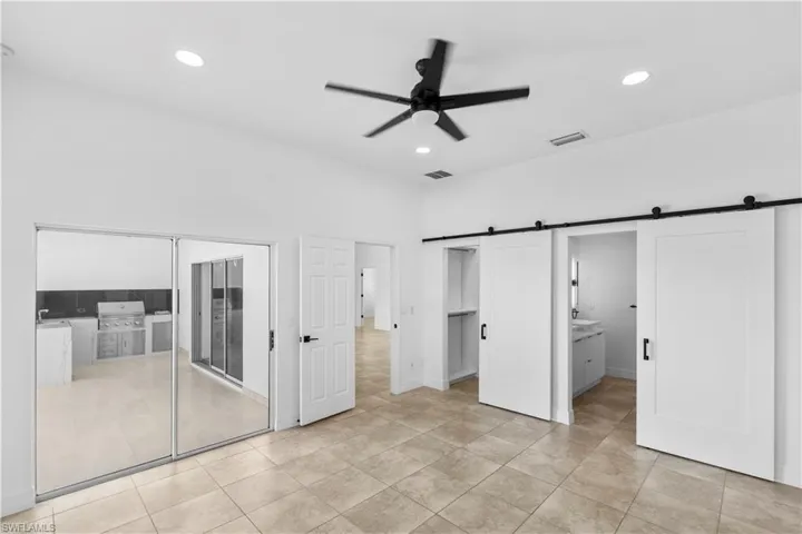 Unfurnished bedroom featuring ensuite bathroom, a barn door, ceiling fan, a closet, and recessed lighting
