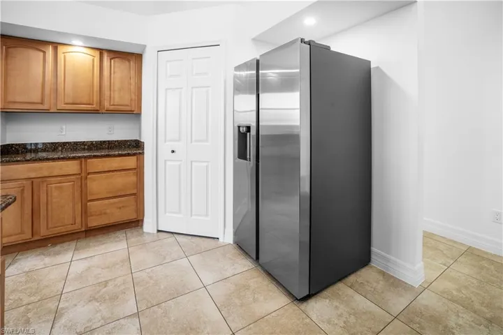 Kitchen with stainless steel refrigerator with ice dispenser, wood finish cabinets, dark stone counters, light tile patterned flooring, and recessed lighting