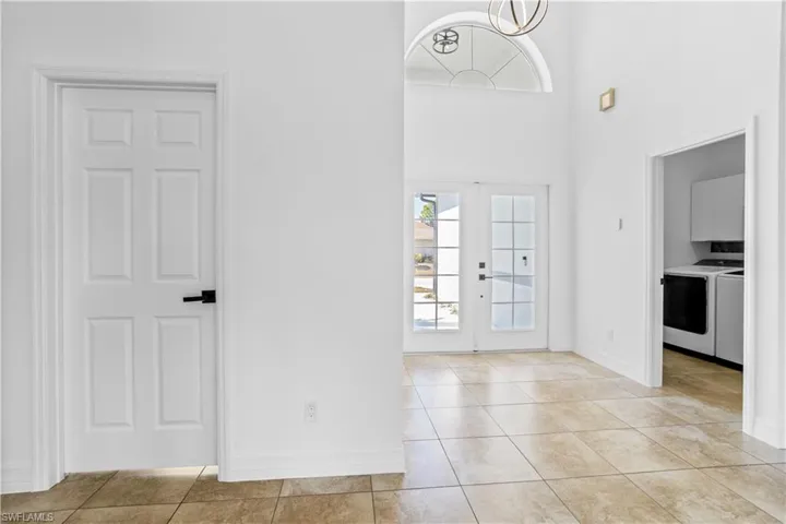 Entryway with healthy amount of natural light, a high ceiling, light tile patterned flooring, french doors, and a chandelier
