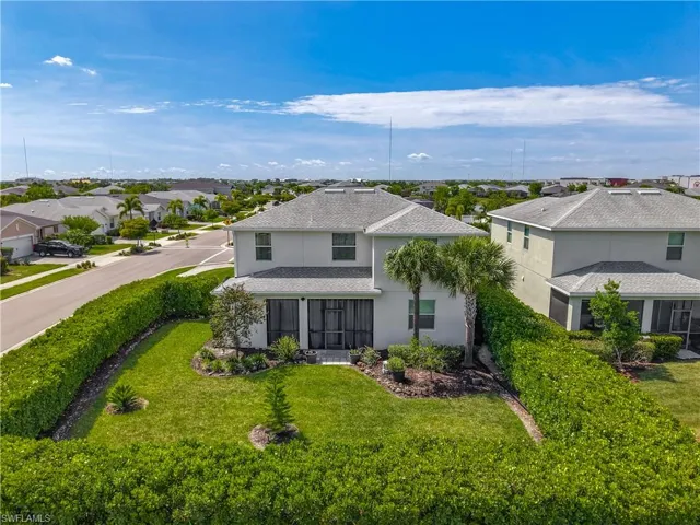 Two-story residence featuring a screened-in patio, mature palm trees, and a manicured lawn