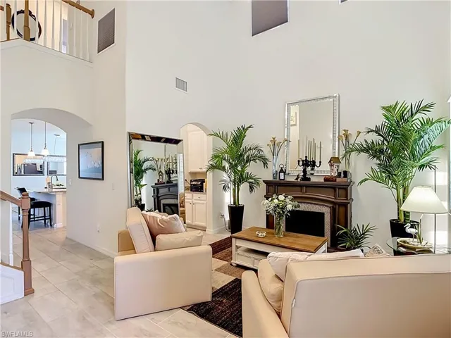 Two-story living area featuring a fireplace with a detailed mantel, high ceilings, arched doorways, and light tile flooring