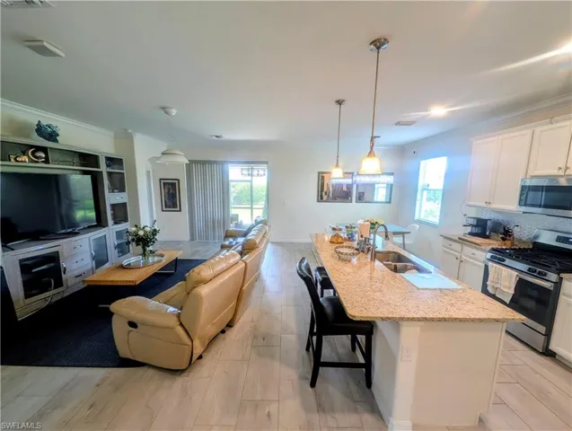 Open-concept living space featuring wood-finish flooring, a kitchen island with stone countertop and integrated sink, stainless steel appliances, white cabinetry, and crown molding