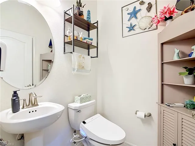 1st half bath room. Pedestal sink with brushed nickel faucet, oval mirror, wall-mounted light fixture, and tile flooring
