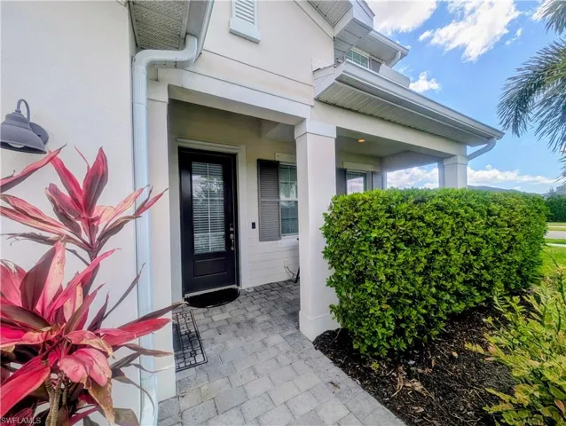 Covered front entryway featuring a brown paneled door with a stucco exterior and a paver walkway