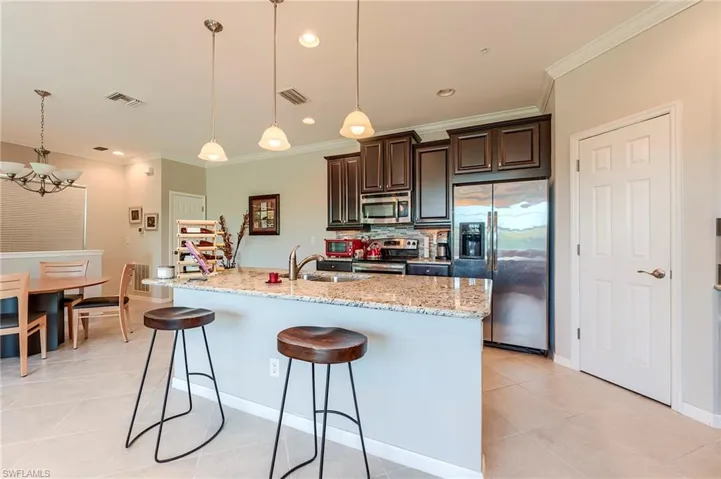 Kitchen featuring appliances with stainless steel finishes, dark brown cabinets, a breakfast bar, decorative light fixtures, and light stone countertops