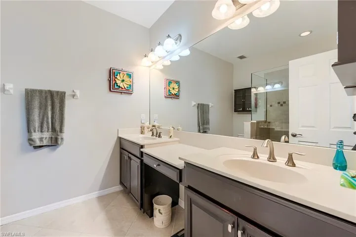 Bathroom featuring double vanity, tiled shower, and light tile patterned flooring