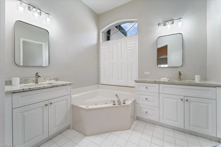 Bathroom featuring a jetted tub, two vanities, and a sink