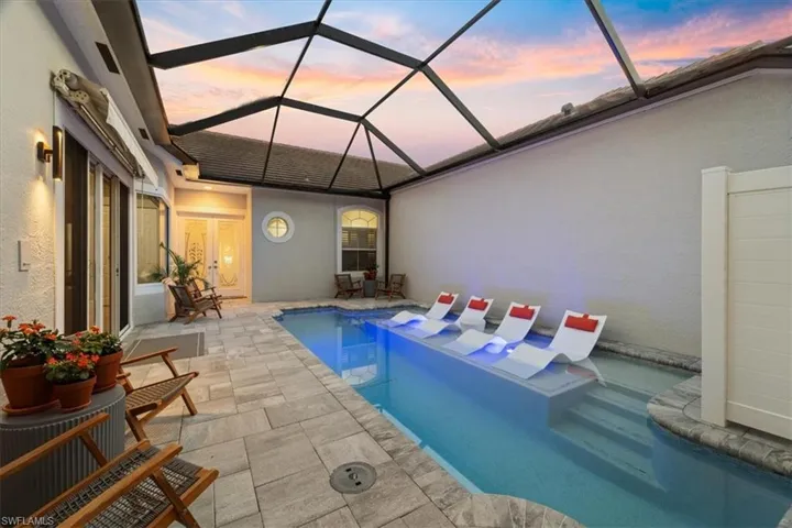 Pool at dusk with glass enclosure, an outdoor pool, and a patio
